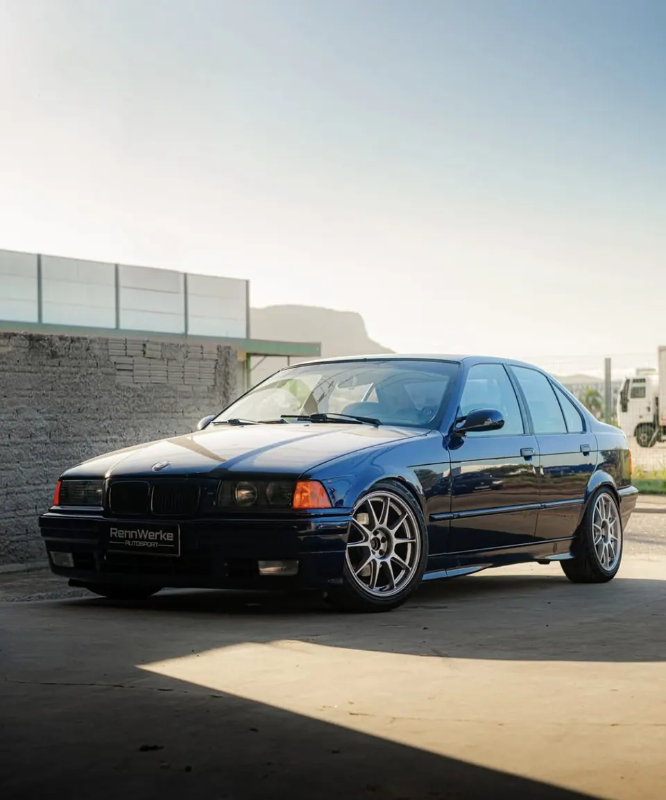 E36 sedã azul com rodas prata estacionada em frente à oficina